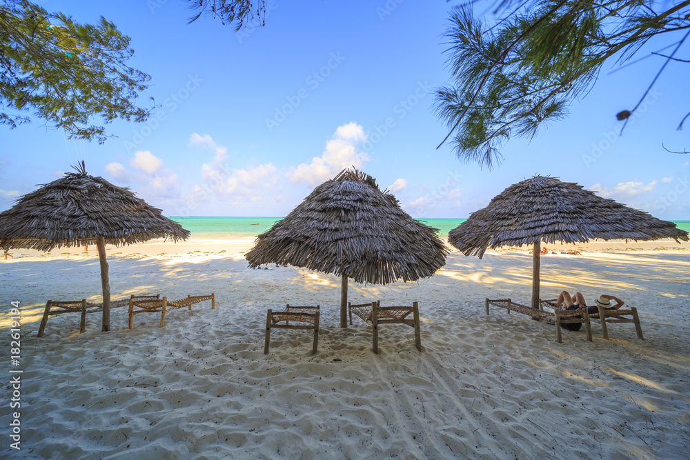 Wooden deck chairs and umbrella on stunning tropical beach. Turquoise blue lagoon of Paje beach, Zanzibar, Tanzania.