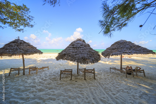 Wooden deck chairs and umbrella on stunning tropical beach. Turquoise blue lagoon of Paje beach, Zanzibar, Tanzania. © pozdeevvs