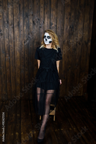 Halloween skull make up girl wear in black against wooden wall at studio.