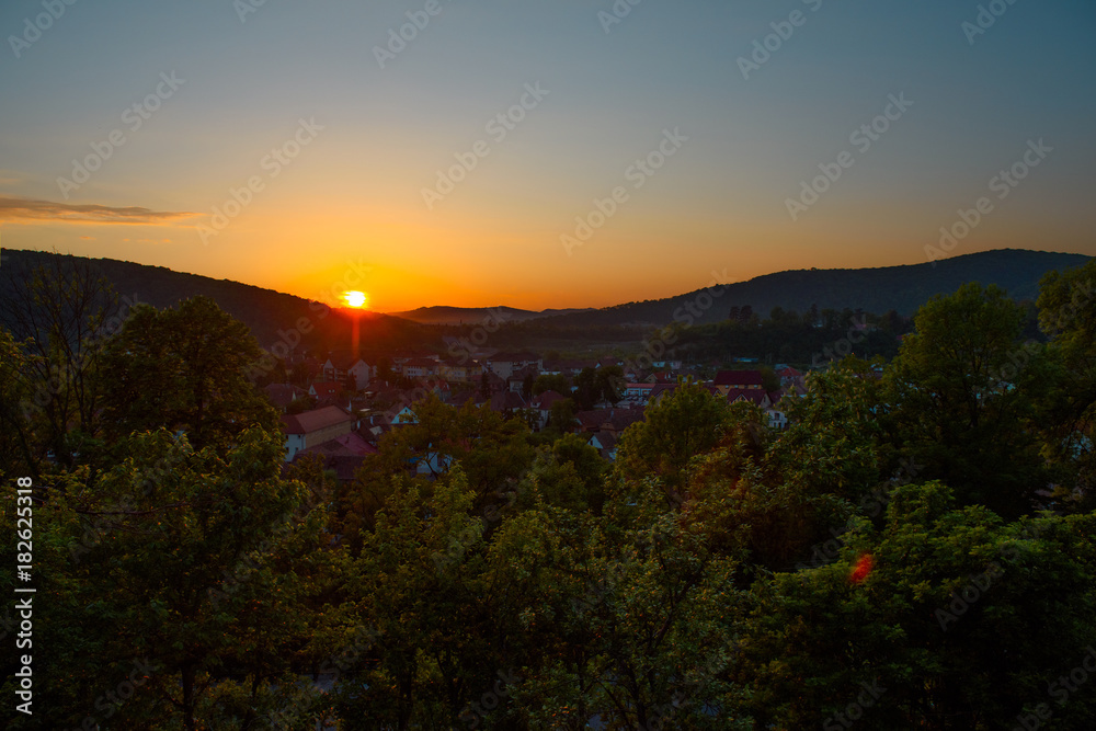 Beautiful landscape of sunrise over small town in forest mountains. Romania, Sighisoara - 2016.