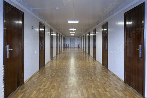 Long office hallway with many doors of dark red wood.