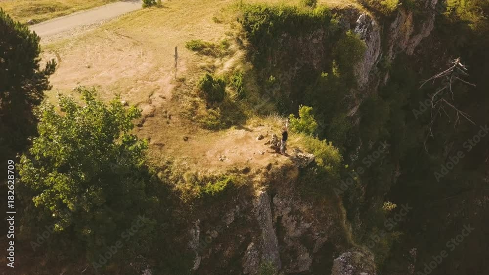 Woman stands at the precipice edge with hands up. Aerial view of cliff face Woman stands at the precipice edge with hands up. Aerial view of cliff face