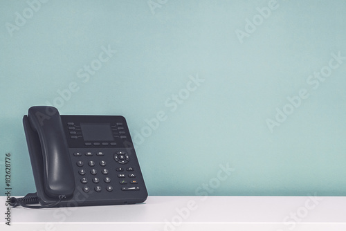 Modern black office phone shot against a blank turquoise wall.