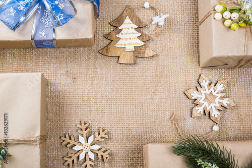 Classy Christmas gifts box presents in brown paper with toys and New Year decor on burlap. Merry christmas card background