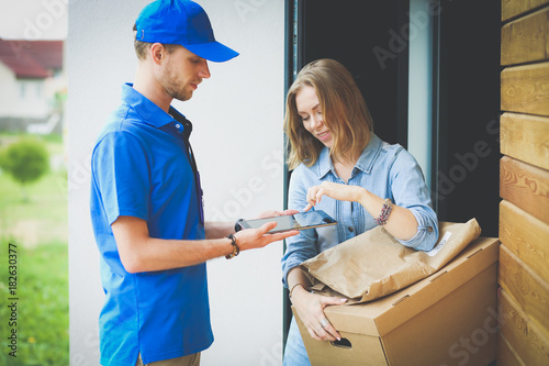Smiling delivery man in blue uniform delivering parcel box to recipient - courier service concept. Smiling delivery man in blue uniform