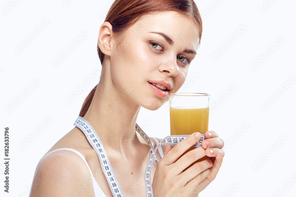 healthy lifestyle, freshly squeezed juice in the hand of a young woman with a measuring tape on a light background portrait healthy lifestyle, freshly squeezed juice in the hand of a young woman with a measuring tape on a light background portrait