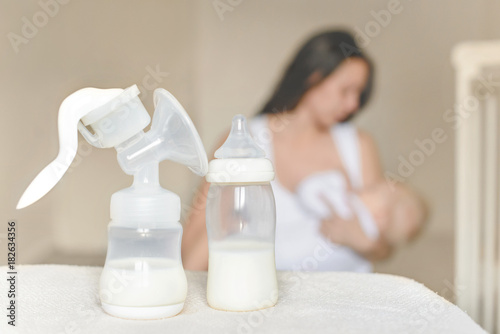 Manual breast pump and bottle with breast milk on the background of mother holding in her hands and breastfeeding baby. Maternity and baby care. photo