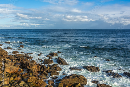 Seashore with rocks, waves,deep blue waters, blue skies with whi