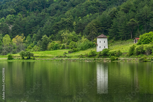 Reflections of green trees and an old windmill into a calm lake