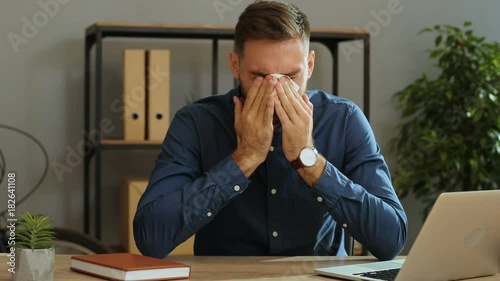 Young sad desperate man crying during his work and usining napkins to removing tears in the office. Close up