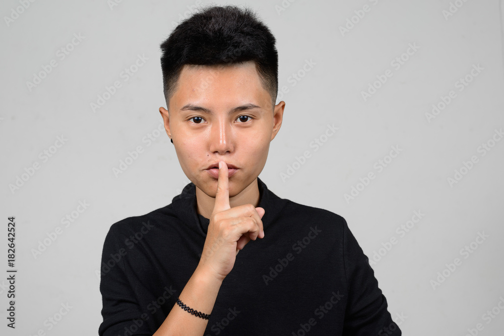 Portrait of Asian young tomboy having secret and holding finger on lips Portrait of Asian young tomboy having secret and holding finger on lips