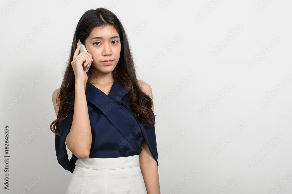 Portrait of young beautiful Asian woman using mobile phone against white background Portrait of young beautiful Asian woman using mobile phone against white background