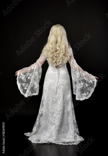 Photography full length portrait of a blonde lady wearing beautiful lace gown, standing pose on black background
