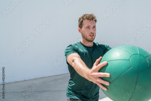 Foto Medicine ball workout fitness man strength training arms doing deltoid front raise exercise for shoulder muscles at gym