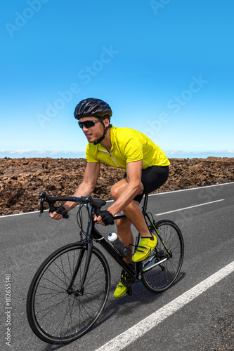 Man biker biking on road race with racing bike. Professional cyclist athlete riding bicycle on competition. Sports equipment, shoes, helmet, gloves, sunglasses. Vertical copy space on blue sky.