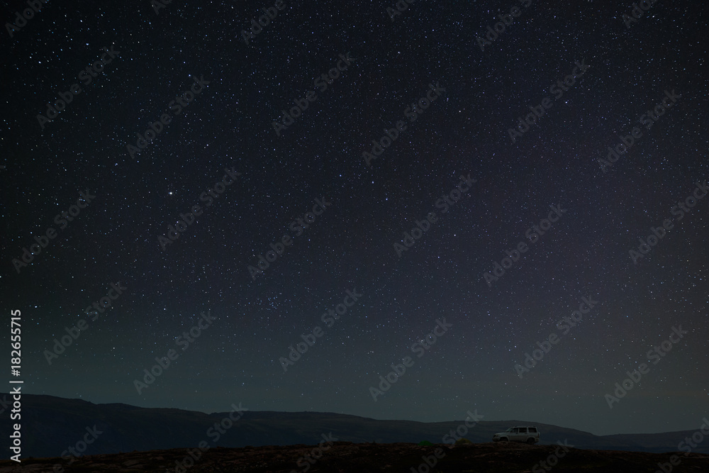 Starry night sky in the mountains above the camp of tourists with a car.