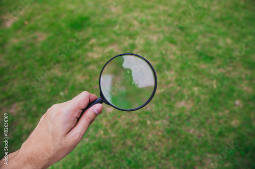 Natural green grass background and magnifier glass in hand. Search concept.