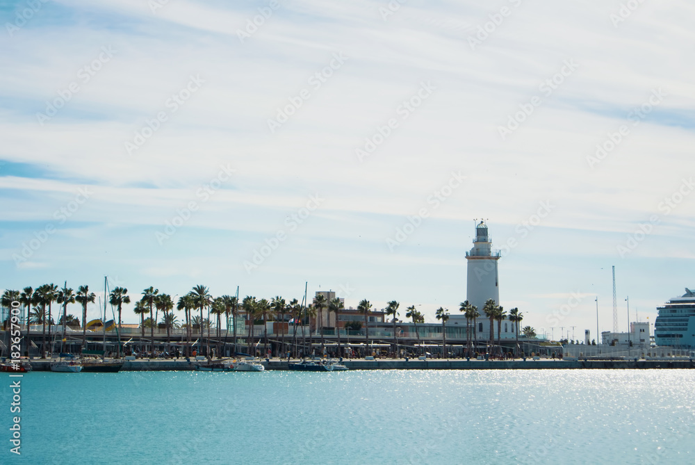 MALAGA, SPAIN - FEBRUARY 7, 2017: A landscape with La Farola lighthouse and a long beautiful promenade with palms, shops and yachts in the water.