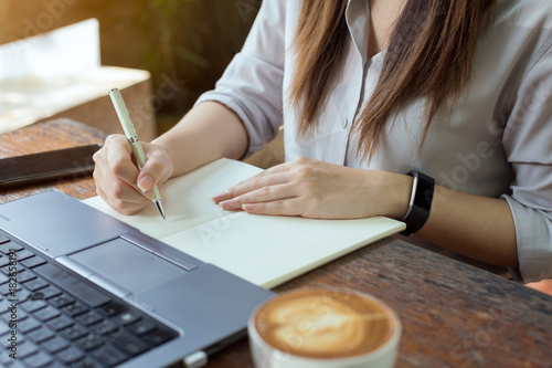Business women using laptop and note some data on notepad, On table is laptop, smartphone and cup of coffee