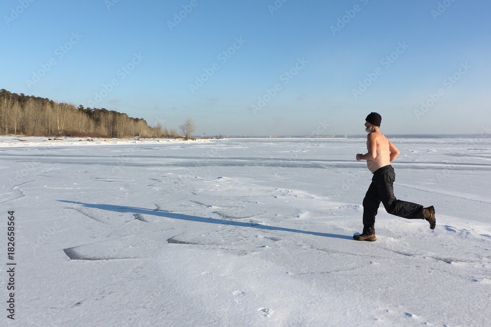 Man in a cap with a naked torso running across the ice of a frozen river, Ob Reservoir, Russia Man in a cap with a naked torso running across the ice of a frozen river, Ob Reservoir, Russia