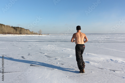 Man in a cap with a naked torso running across the ice of a frozen river, Ob Reservoir, Russia