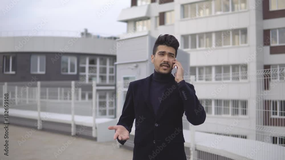 Handsome young business man talking on smartphone and walking away smiling happy wearing suit jacket outdoors. Handsome young business man talking on smartphone and walking away smiling happy wearing suit jacket outdoors.