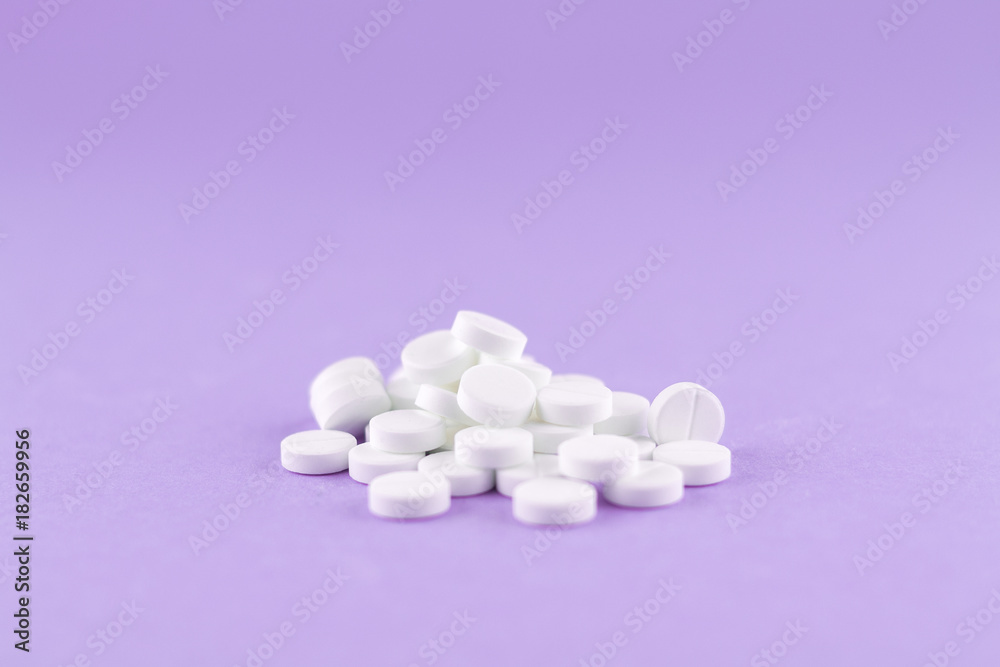 Close up white pills on purple background with copy space. Focus on foreground, soft bokeh. Pharmacy drugstore concept