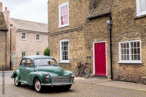 Retro scene with vintage British car 1950 style parked in front of Victorian English building with red door.