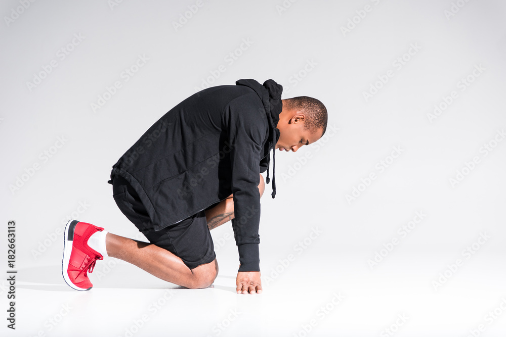 side view of young african american sportsman in hoodie kneeling isolated on grey side view of young african american sportsman in hoodie kneeling isolated on grey
