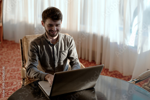 Smiling bearded hipster-guy, keyboarding in network on a laptop. photo