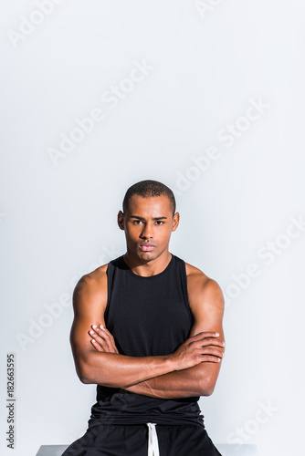 confident young african american sportsman with crossed arms looking at camera isolated on grey