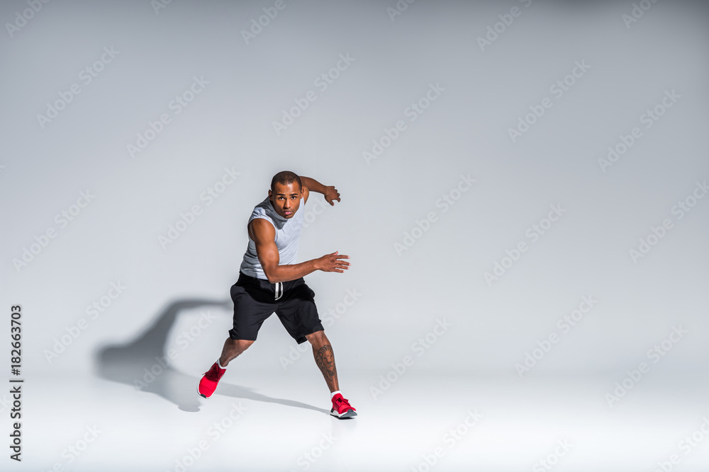 full length view of athletic young african american sportsman looking at camera on grey