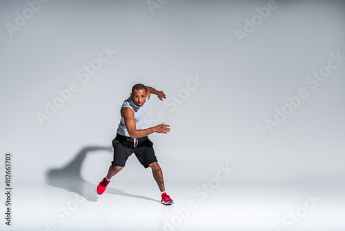 full length view of athletic young african american sportsman looking at camera on grey