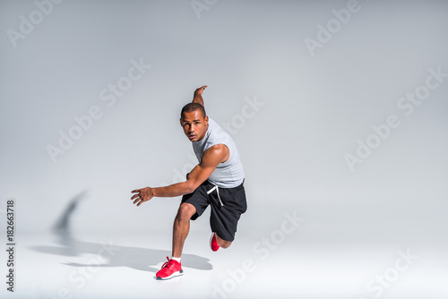 young african american sportsman running and looking at camera on grey