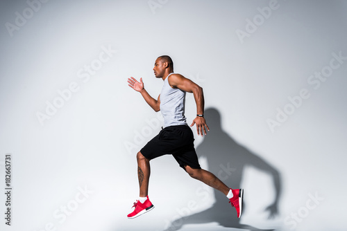 side view of young african american sportsman running on grey