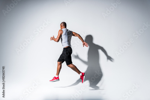 full length view of young african american sportsman running on grey