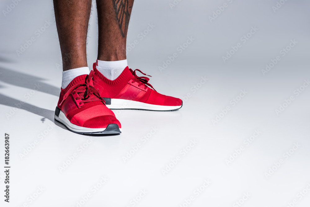 close-up partial view of african american man in sports shoes standing isolated on grey