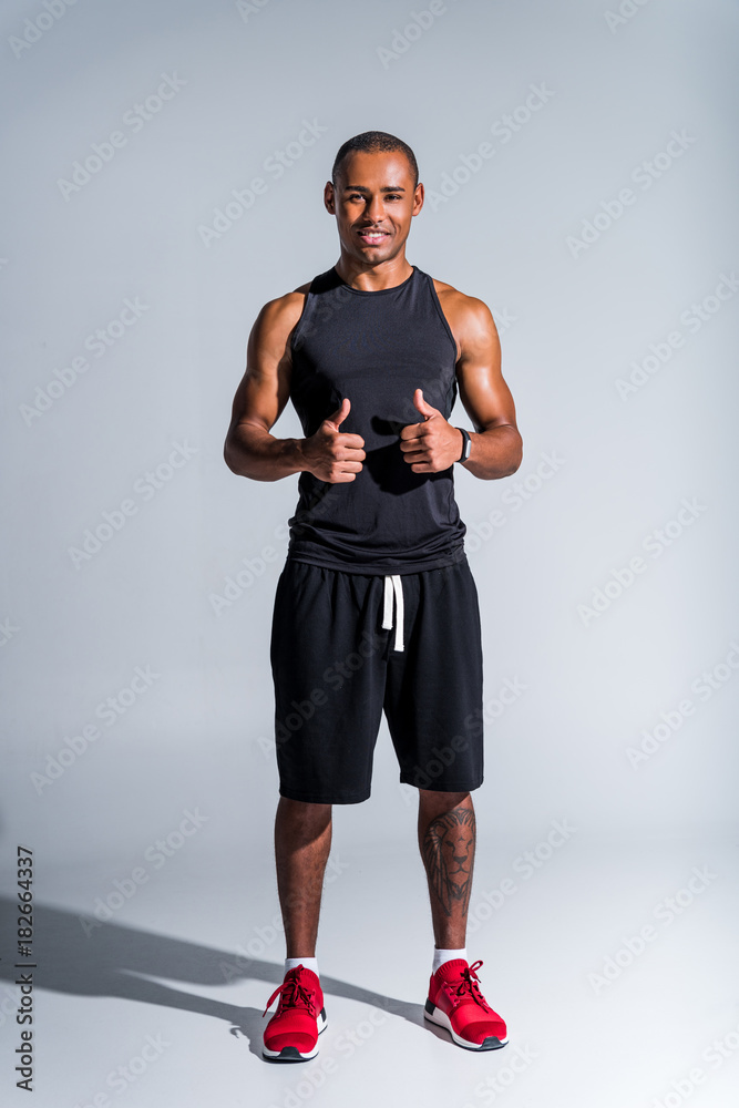 cheerful african american sportsman showing thumbs up and smiling at camera isolated on grey cheerful african american sportsman showing thumbs up and smiling at camera isolated on grey