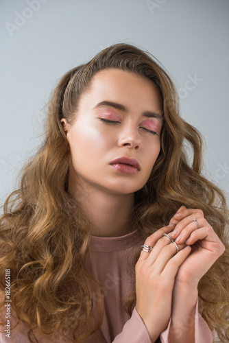 portrait of beautiful girl with makeup and rings with closed eyes isolated on gray