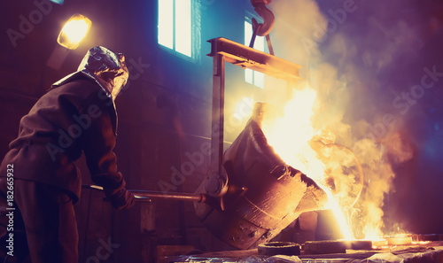 Worker controlling metal melting in furnaces. Workers operates at the metallurgical plant. The liquid metal is poured into molds.