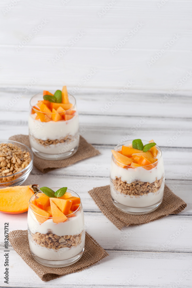 Persimmon creamy trifle in beautiful glasses, fresh ripe fruit slices on white wooden background. Healthy vegetarian food. Delicious dessert. Close up photography. Selective focus. Persimmon creamy trifle in beautiful glasses, fresh ripe fruit slices on white wooden background. Healthy vegetarian food. Delicious dessert. Close up photography. Selective focus.