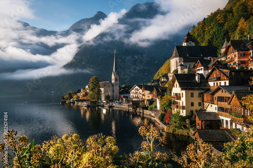 Scenic view of famous Hallstatt lakeside town reflecting in Hallstattersee lake in the Austrian Alps in morning light in autumn with bushes and flowers on the foreground, Salzkammergut region, Austria