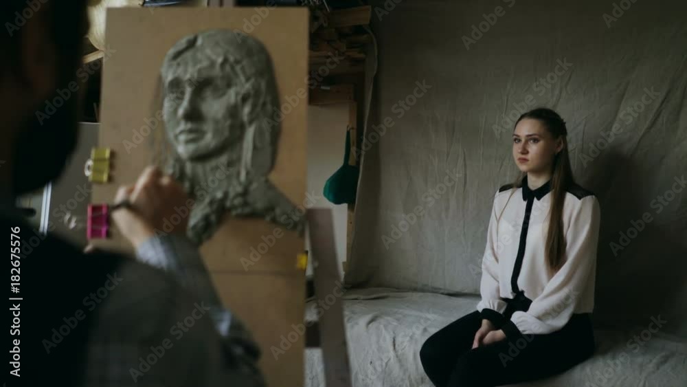 Skilled sculptor works with plasticine on canvas to create woman's face of posing model in art studio Skilled sculptor works with plasticine on canvas to create woman's face of posing model in art studio