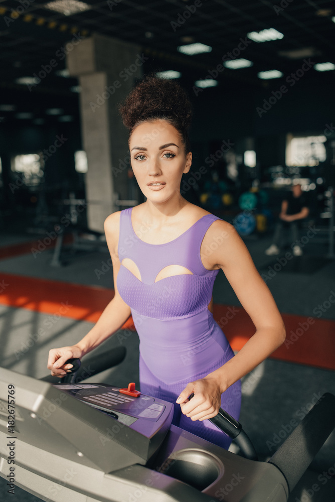 Gym woman working out happy sitting by moonwalker fitness machines. Beautiful fit young mixed race female fitness model inside in fitness center. Gym woman working out happy sitting by moonwalker fitness machines. Beautiful fit young mixed race female fitness model inside in fitness center.