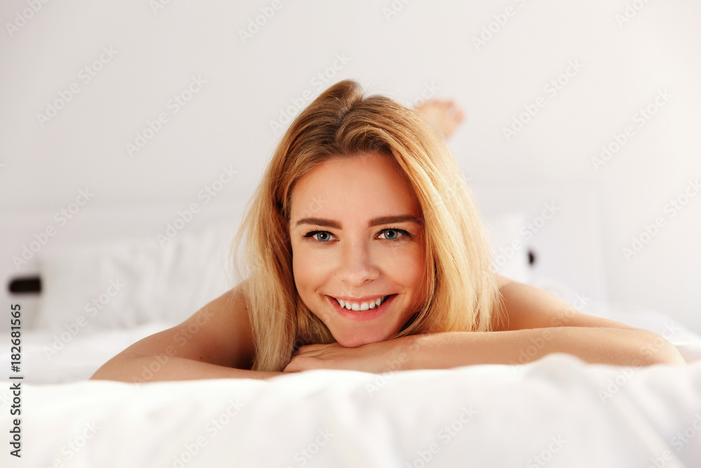 Fototapeta premium Dreamy blonde woman lies on white bed early in the morning