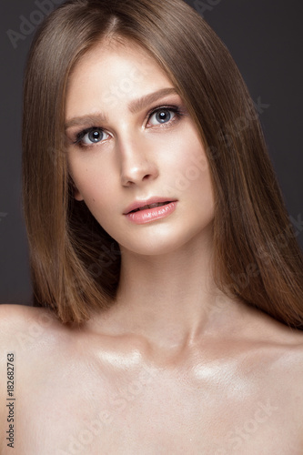 Beautiful young girl with a light natural make-up and perfect skin. Beauty face. Picture taken in the studio on a grey background.