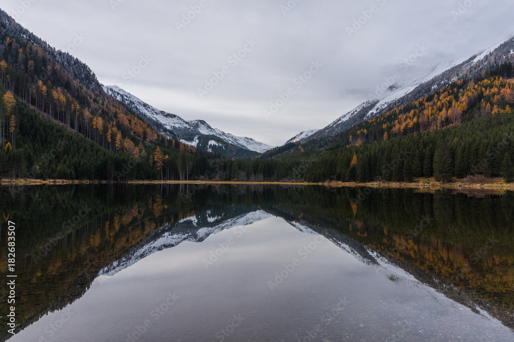 Autumn colored forest and snow covered mountains reflecting in the cold waters of Ingeringsee