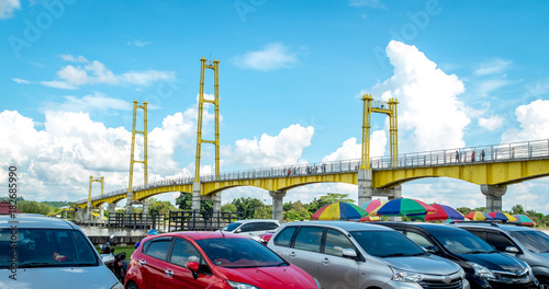 cars parking near pedestrian bridge crossing Mahakam River in Pulau Kumala, Tenggarong, Indonesia photo