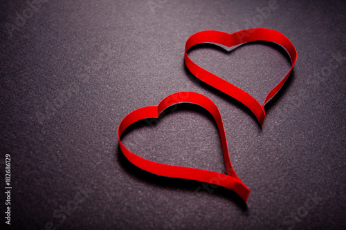 Valentine's day card. Couple of red hearts made of ribbon on black background with copy space.