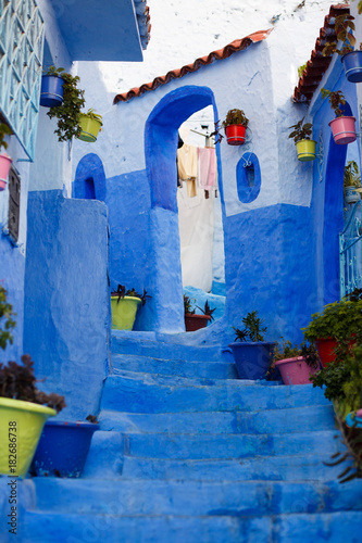 Colorful vases with plants stand on blue footsteps on blue street somewhere in Morocco © IVASHstudio